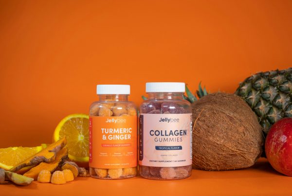 Two bottles of gummy supplements labeled “Turmeric & Ginger” and “Collagen Gummies” are placed on an orange background, surrounded by fresh fruits like orange slices, pineapple, coconut, and an apple.